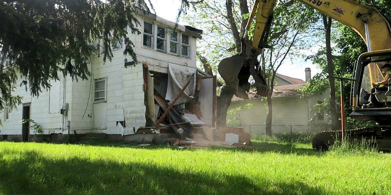 Backhoe demoing small room on back of a House